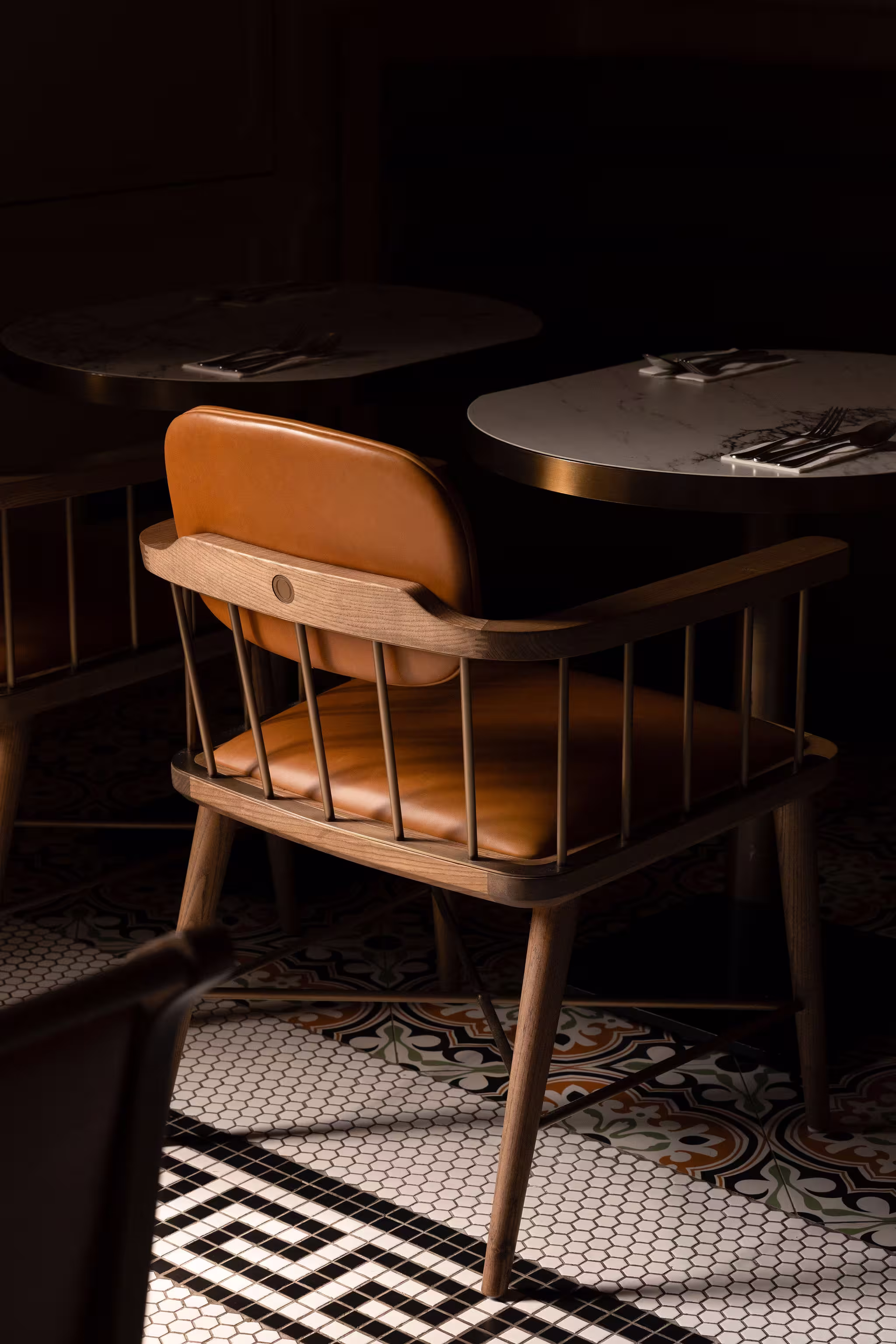 Wooden chair with brown leather cushions beside a round marble table set with cutlery in a dimly lit restaurant.