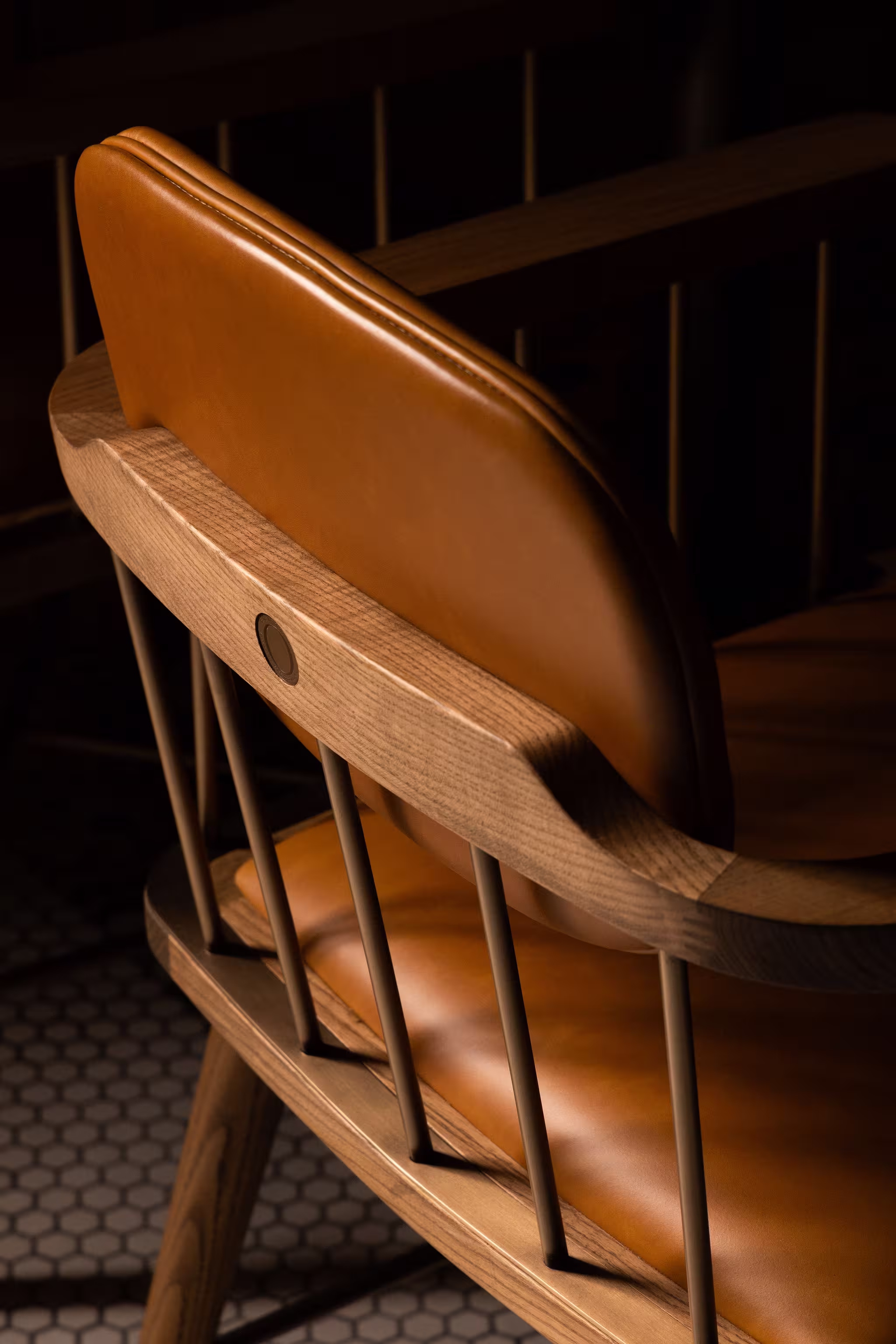 Close-up of a wooden chair with tan leather cushioning and vertical metal rods in a dimly lit room.