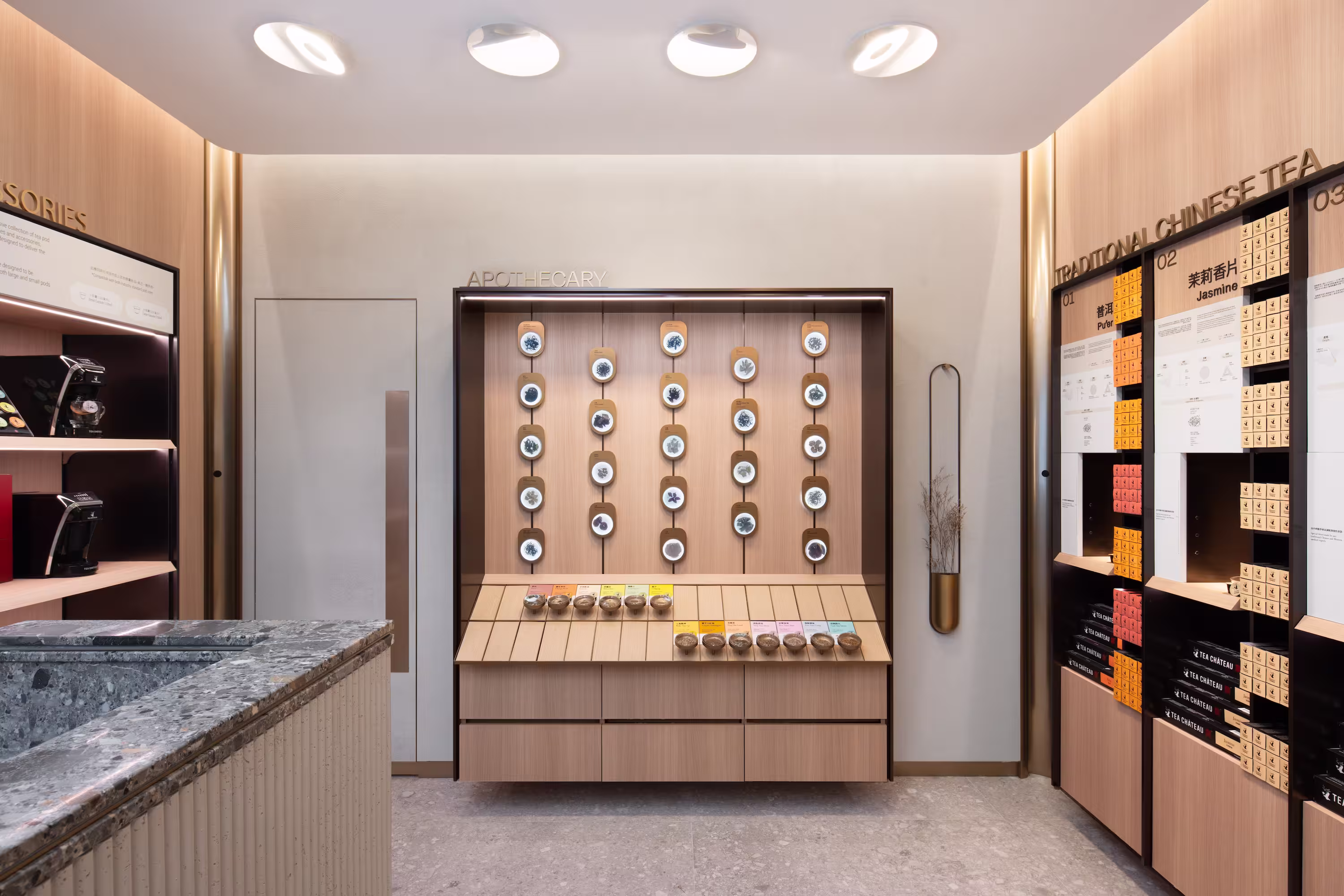 Tea Chateau circular hero display detail with concentric brass rings, glass shelves, brewed tea vessels, and tropical greenery