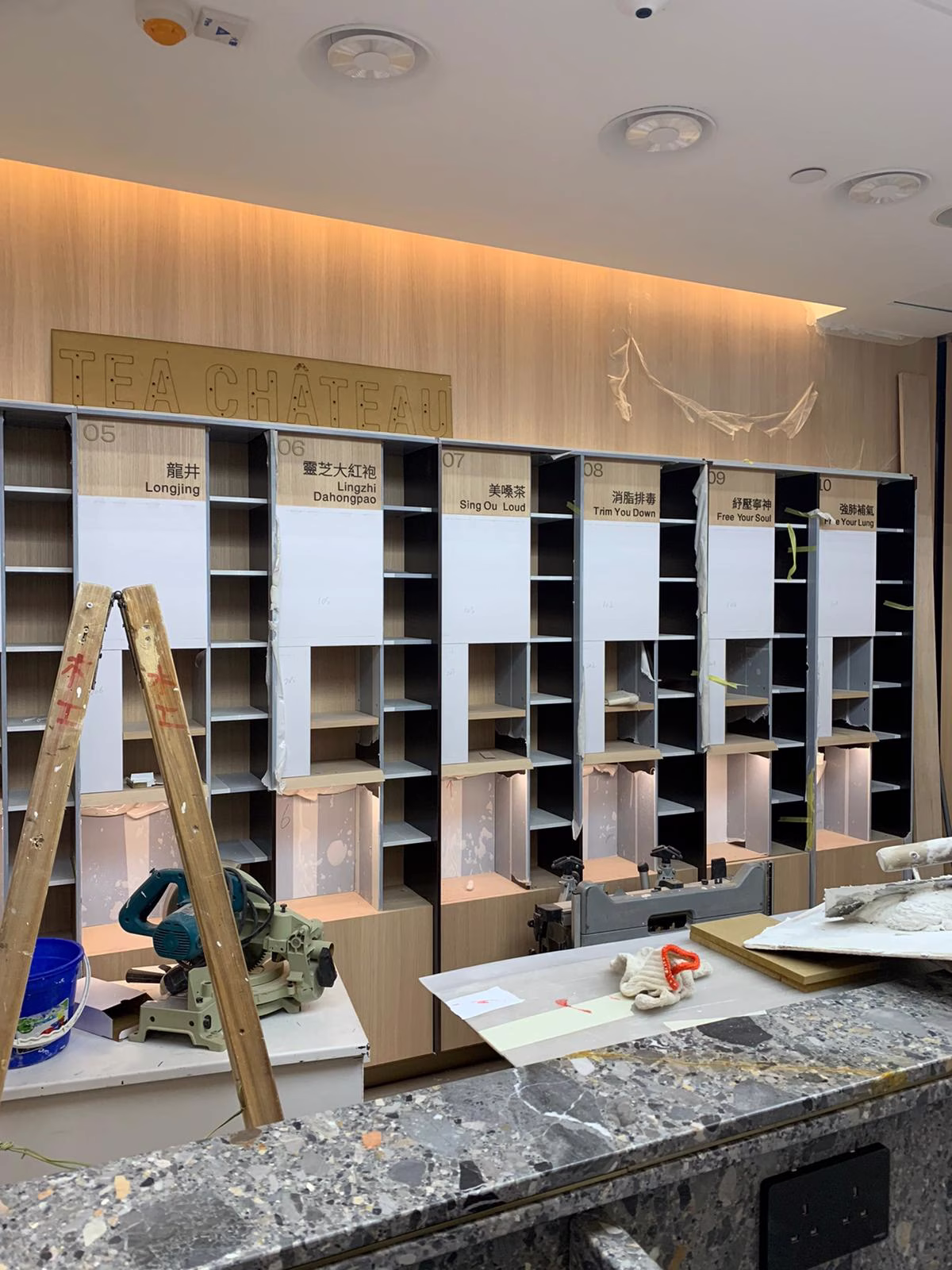 Construction progress photograph of Tea Chateau showing apothecary wall illumination testing with backlit resin-encased tea ingredient pods