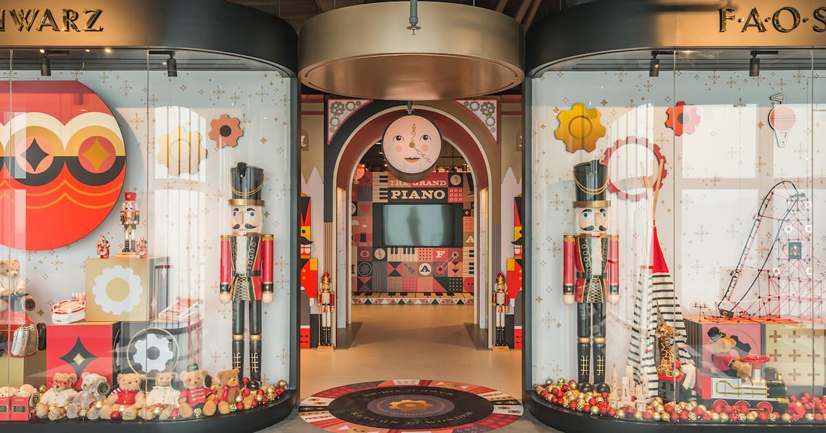 Decorative toy store window display featuring nutcracker soldiers, teddy bears, and colorful geometric patterns with a grand piano area inside.