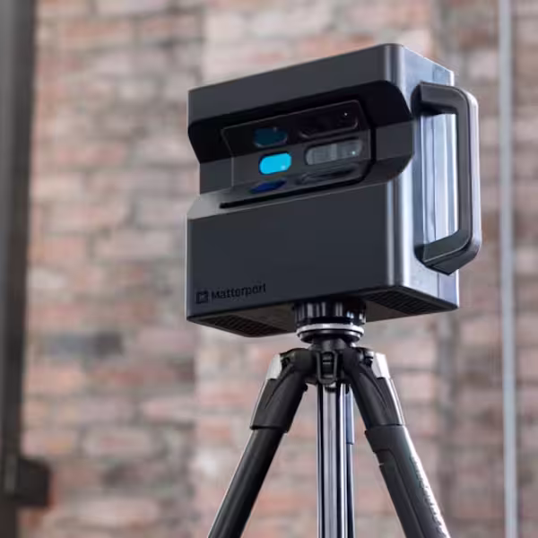 Katterport 3D camera mounted on a black tripod against a blurred brick wall background.