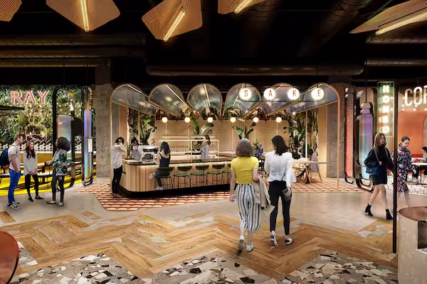 Modern indoor bar area with people walking and socializing under soft warm lighting, featuring a curved wooden counter and decorative ceiling mirrors.