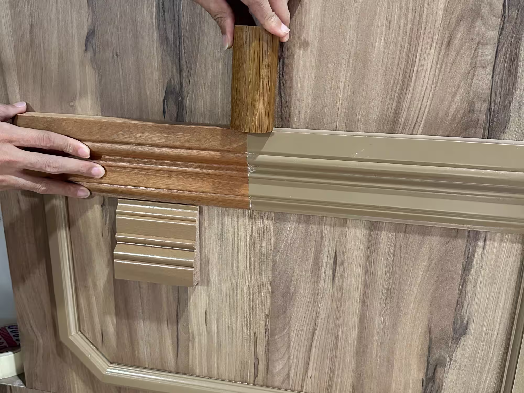 Person fitting wood-patterned molding pieces together on a wooden surface.