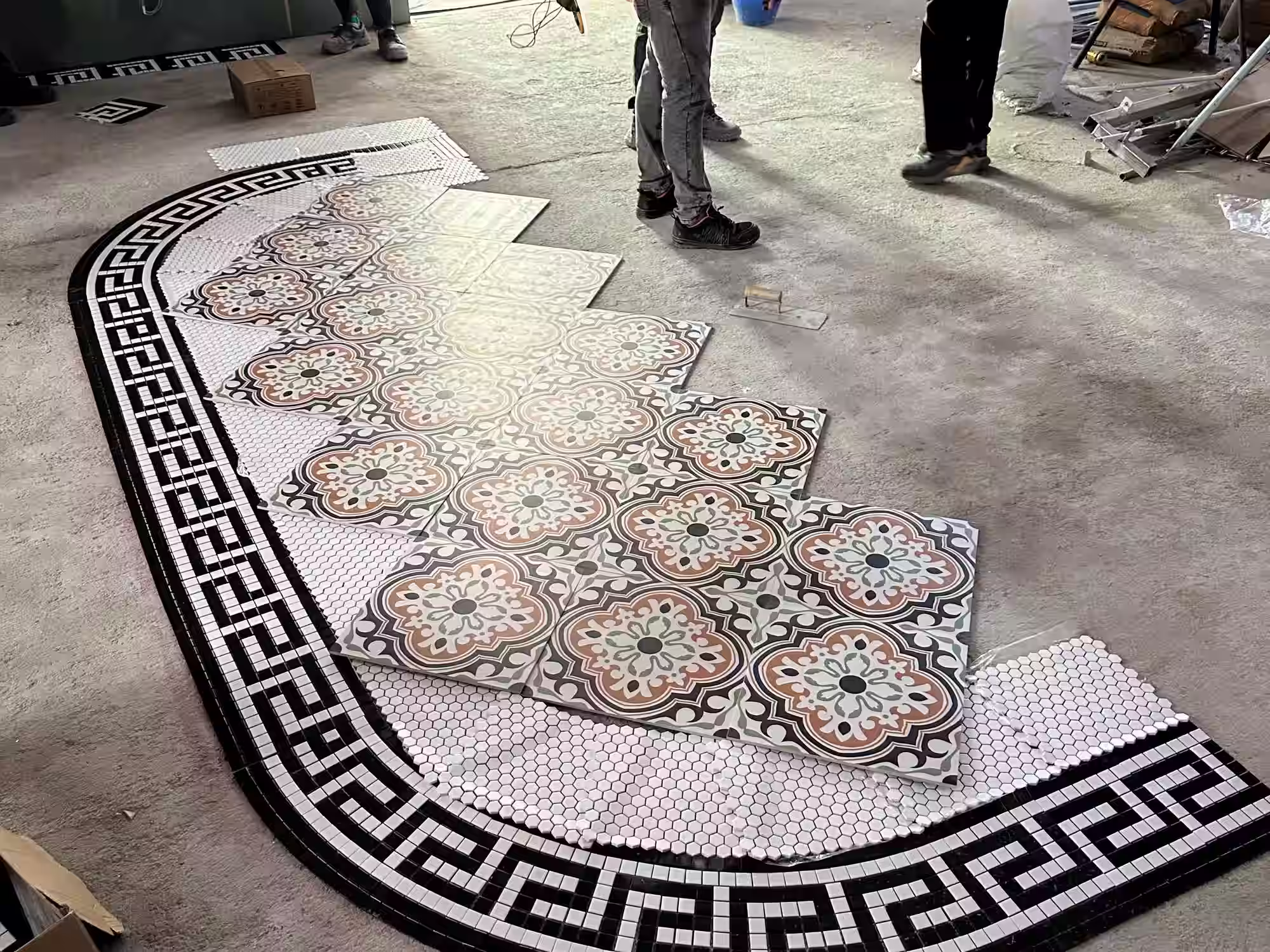 Partially installed decorative floor tiles with floral center pattern and black and white border in a curved layout.