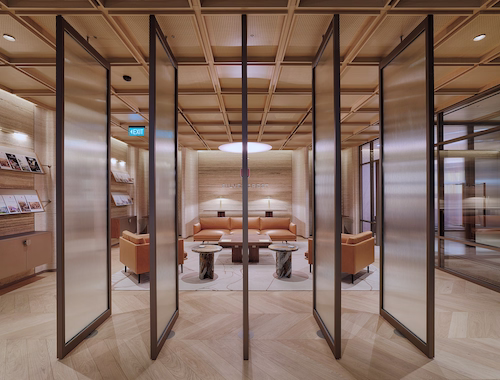 Bronze-framed glazed doors folded open onto a lounge of curved banquettes and round tables under an oval pendant