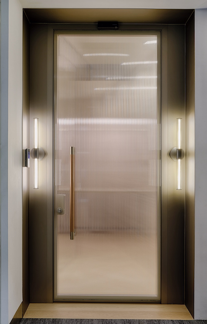 The entrance door in reeded glass and bronze, flanked by two vertical light strips