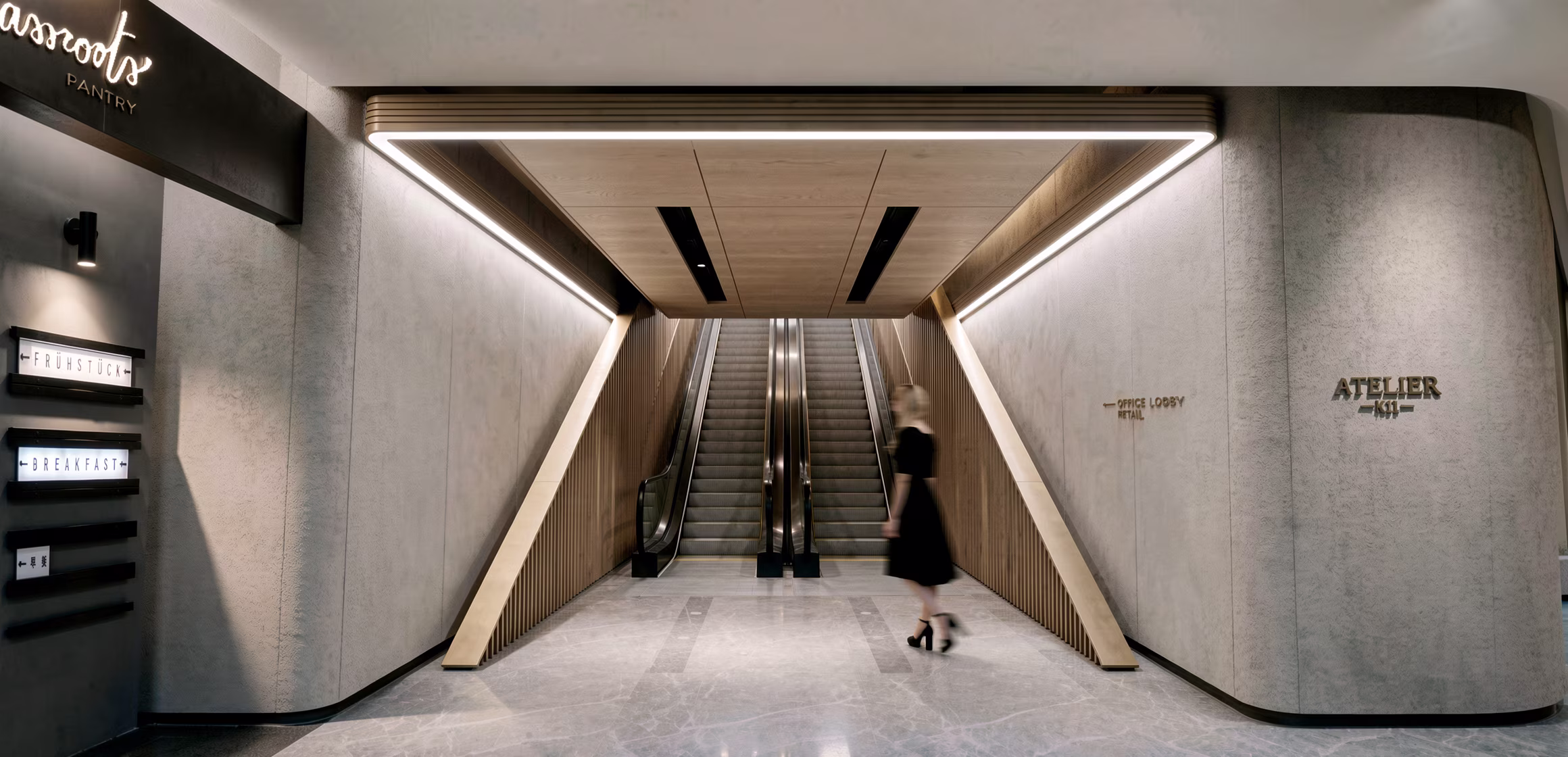 Escalator hall linking the podium retail to the office lobby, with wayfinding cut into the stone wall
