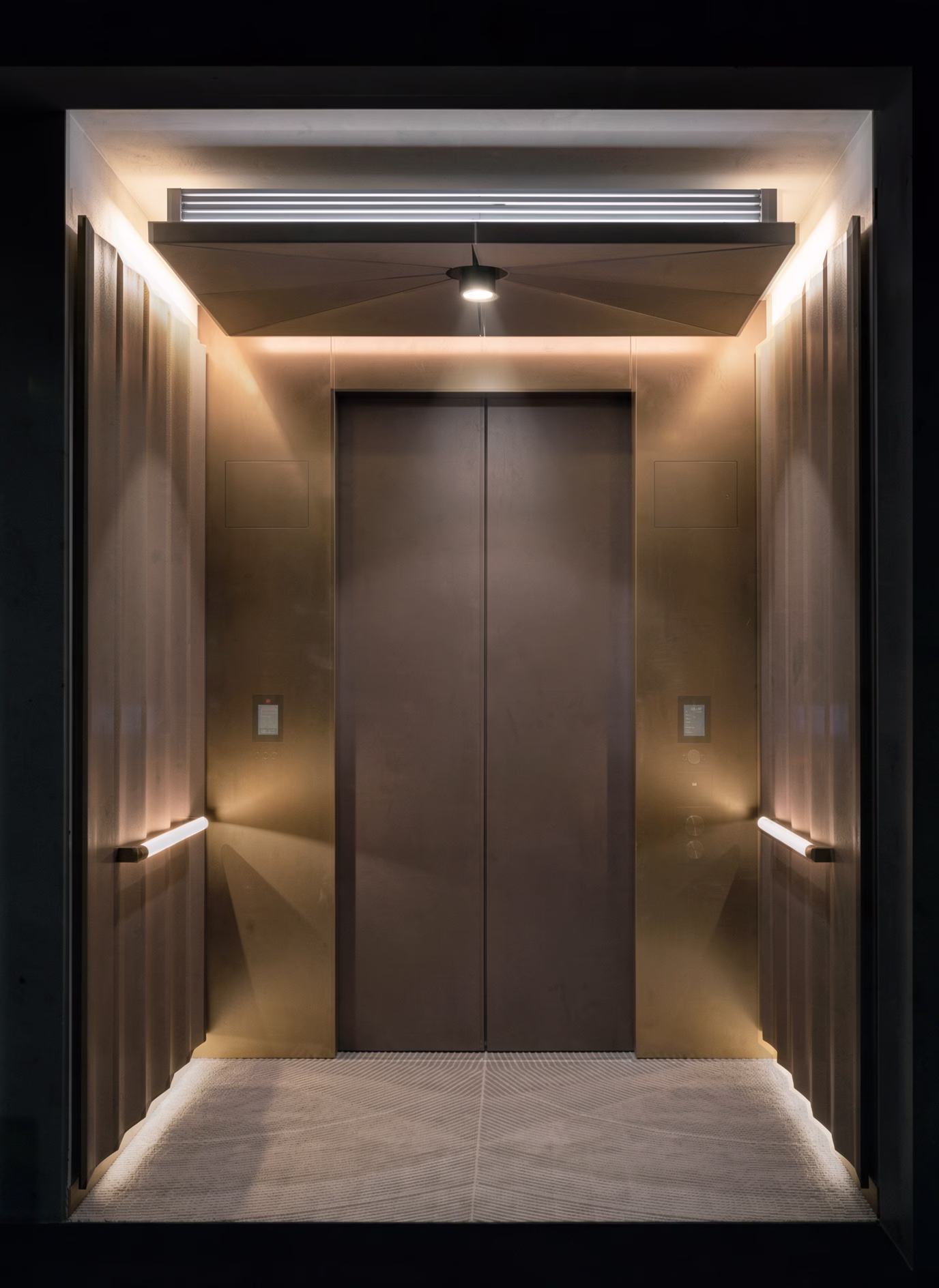 Lift lobby with bronze doors framed by fluted metal panels and a faceted lit ceiling