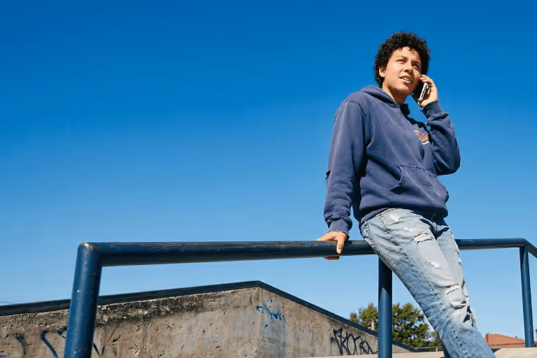 Young man leaning on a blue railing talking on a smartphone