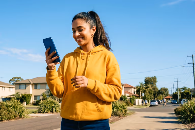 Smiling woman looking at her smartphone while standing on a suburban street