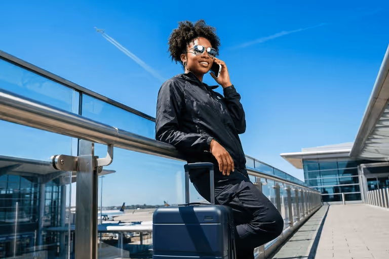 Woman leaning on a suitcase at an airport terminal while talking on her phone