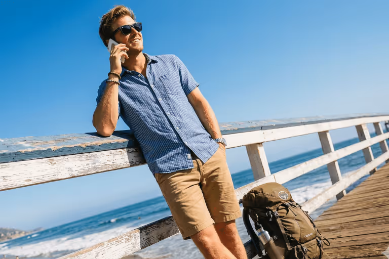 Man talking on a phone while leaning against a wooden pier railing by the ocean
