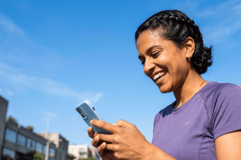 Smiling woman in purple athletic shirt looking at her smartphone outdoors
