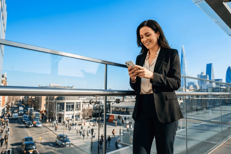 Smiling woman standing on a balcony using her smartphone