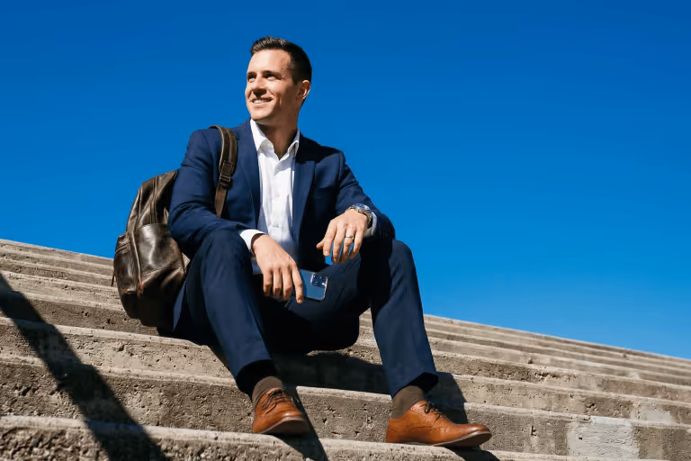 A smiling man sitting on concrete steps holding a smartphone