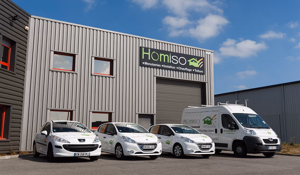Façade d'un bâtiment industriel avec le logo Homiso, quatre véhicules blancs de l'entreprise stationnés devant.