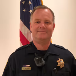 Police officer in uniform standing in front of an American flag.