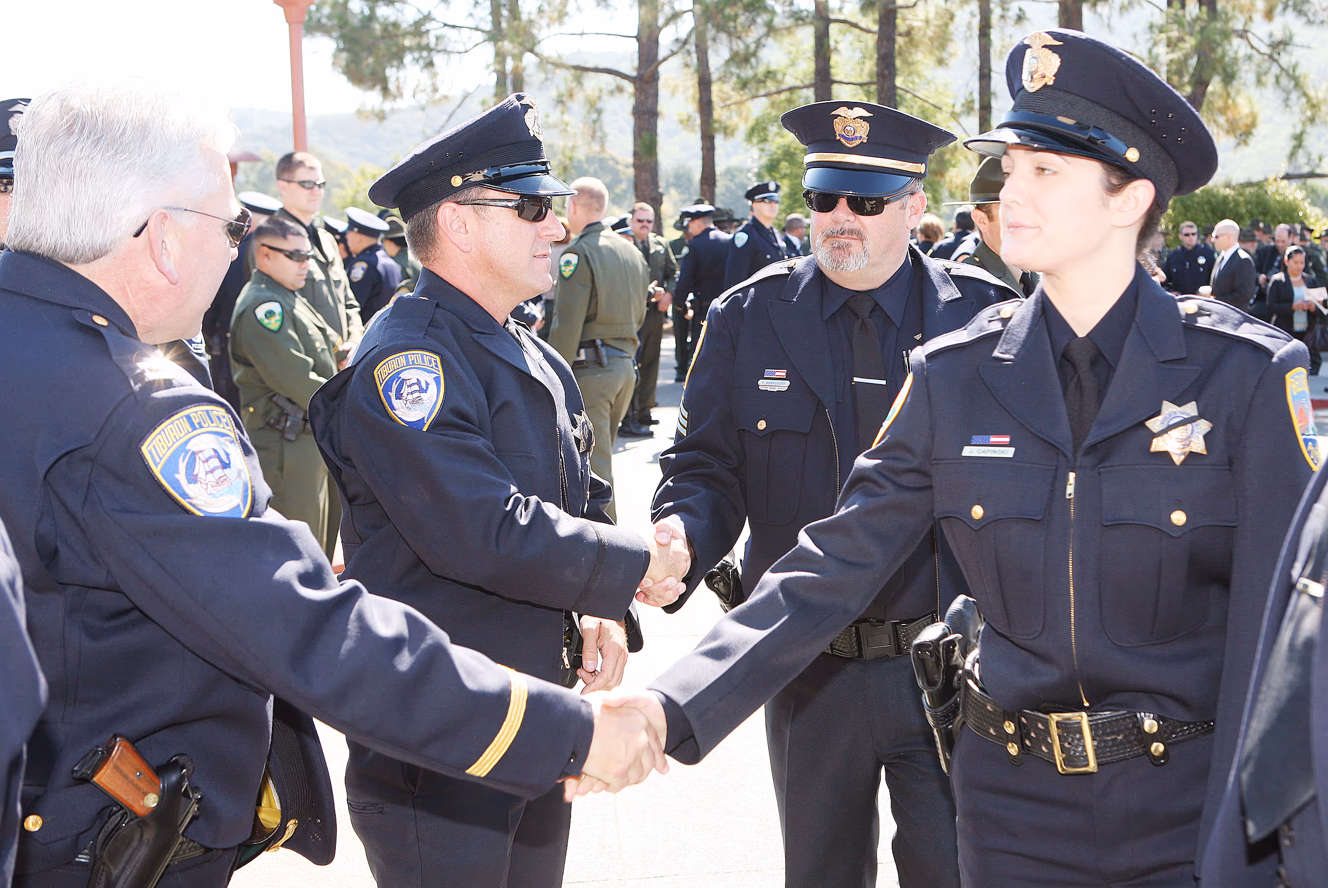Police officers in uniform shaking hands outdoors during a formal gathering or ceremony in bright daylight.