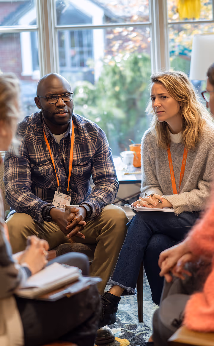 A diverse group of adults engaged in a serious discussion in a cozy room with large windows.