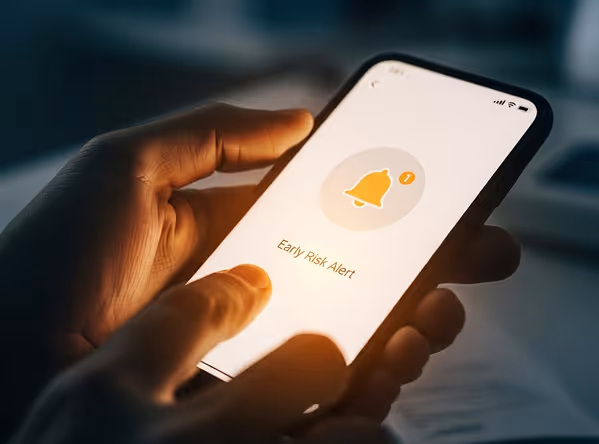 Hand holding smartphone displaying an Early Risk Alert notification with a bell icon and a '1' badge.