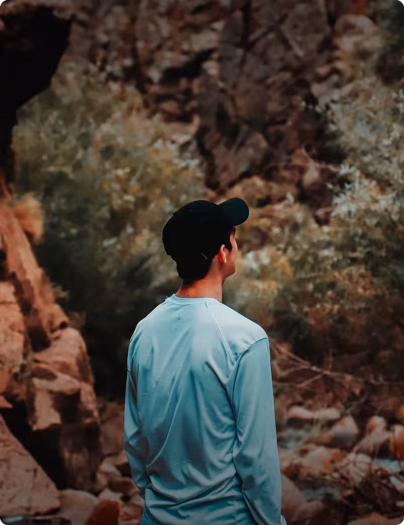 a relaxed young man facing away from the camera looks out over a scene in nature