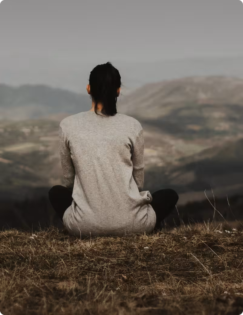 woman sitting on a hill overlookinga valley and mountains