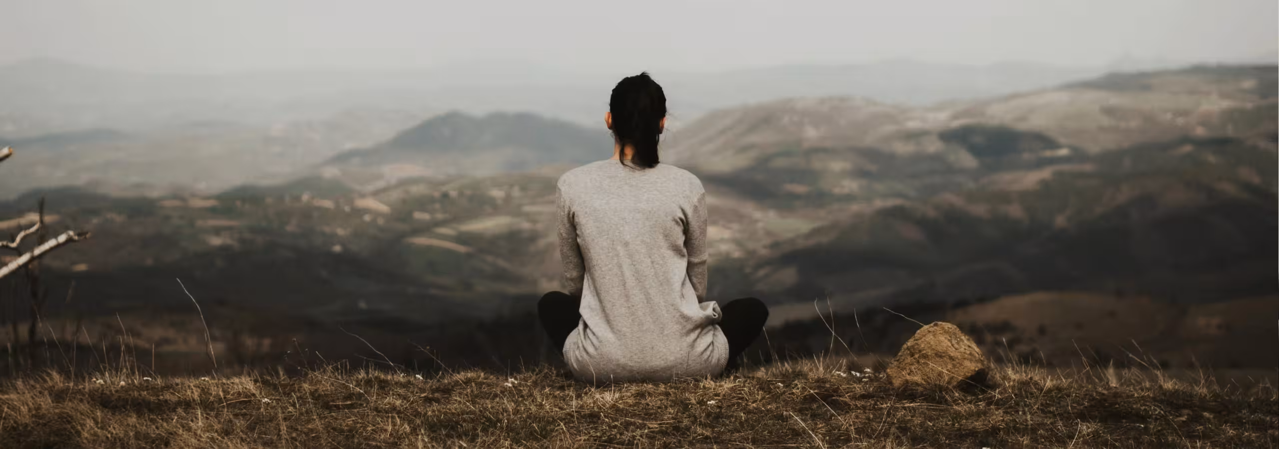 woman sitting on a hill overlookinga valley and mountains