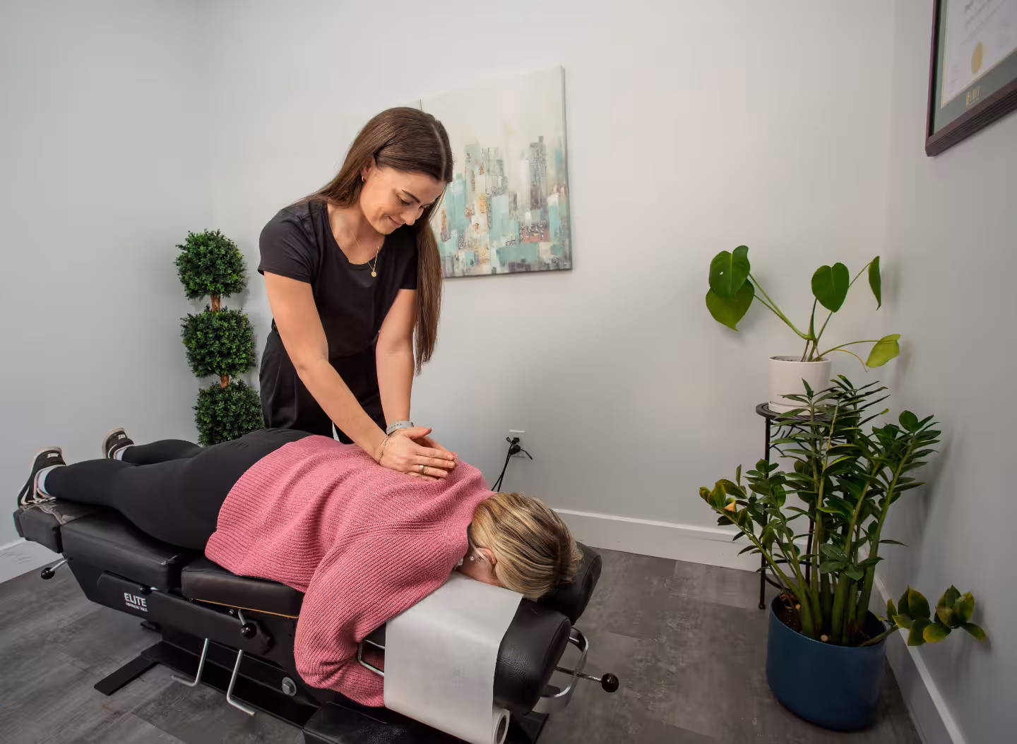 female chiropractor adjusts a patient lying face down on a black chiropractor's table