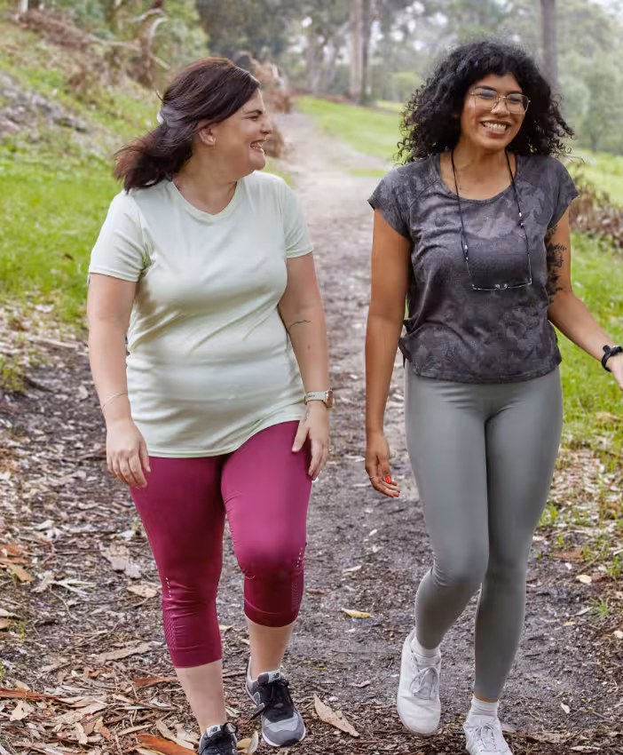 Two women smiling and laughing as they walk on a path in a park