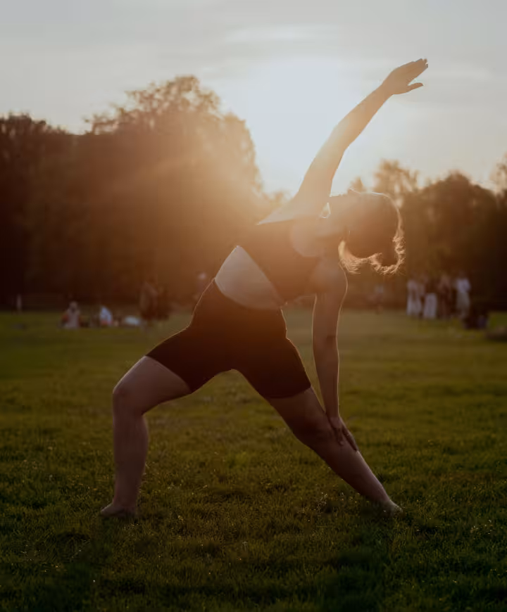 Woman in a yoga pose with the rising sun behind her