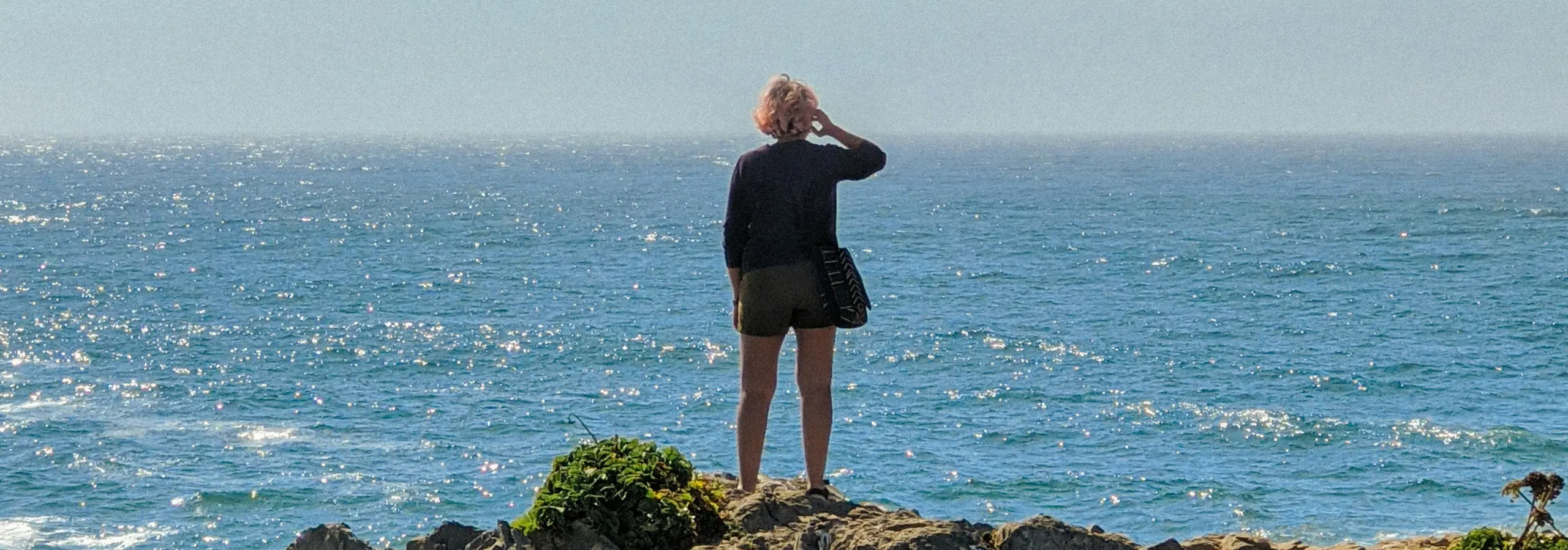 woman standing on a rocky shoreline looking out to sea