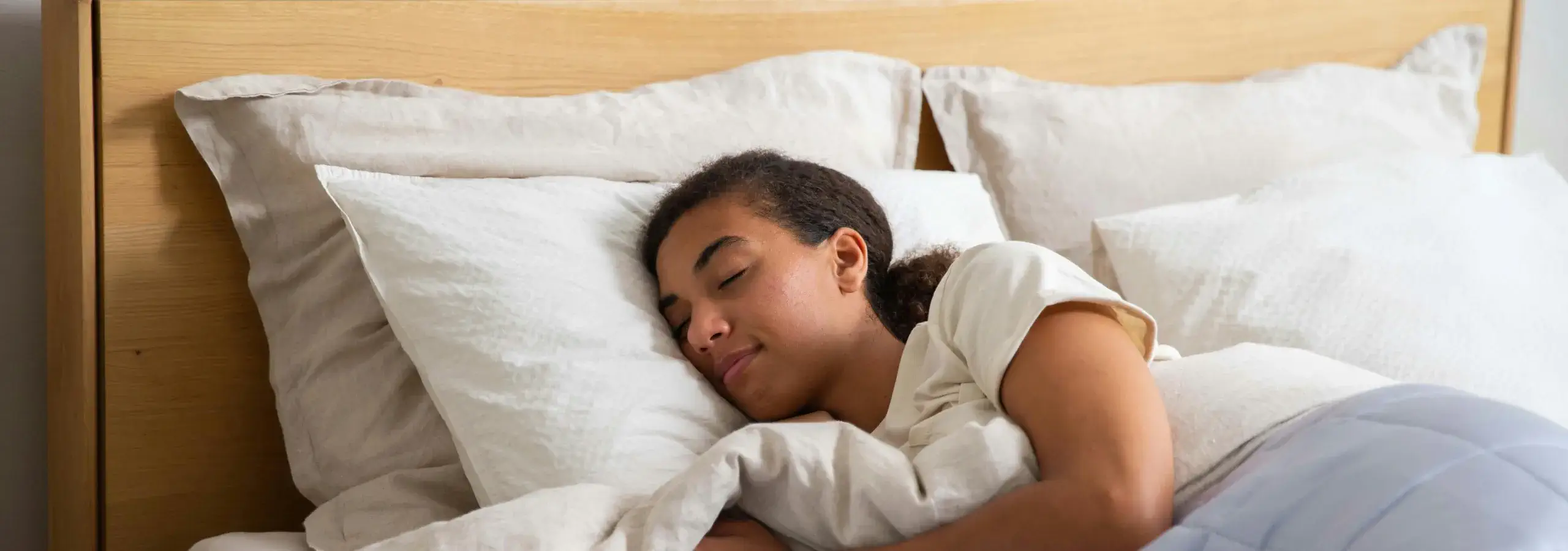 A young woman sleeping peacefully in a comfortable bed with white pillows and bedding.
