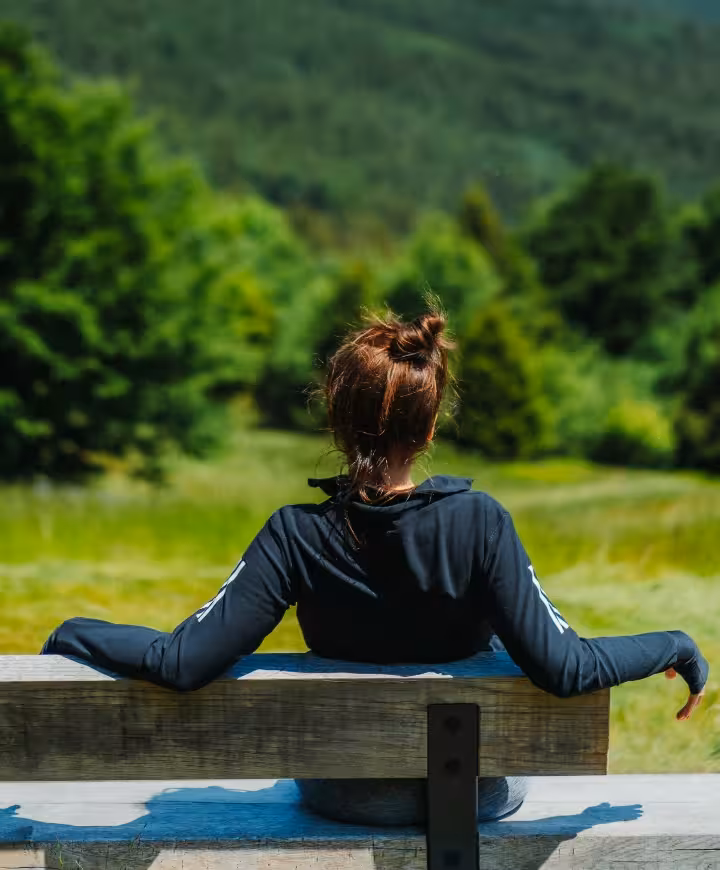A rear view of a relaxed woman sitting on a bench looking at trees
