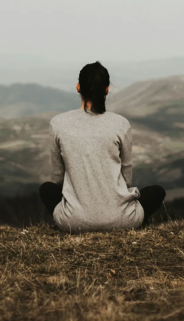 woman sitting on a hill overlookinga valley and mountains