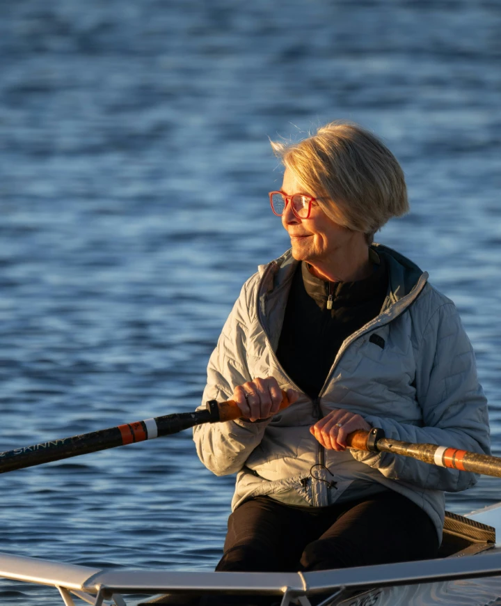 Woman in a rowboat on a lake with the setting sun lighting her face.
