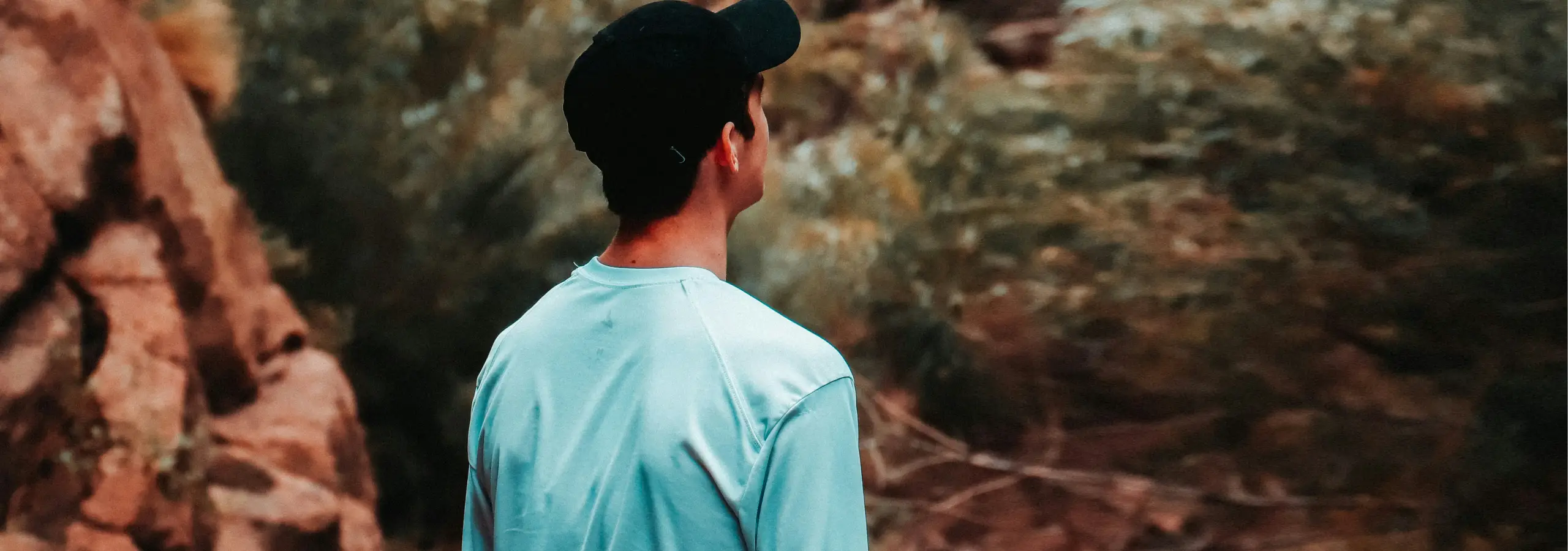 a relaxed young man facing away from the camera looks out over a scene in nature