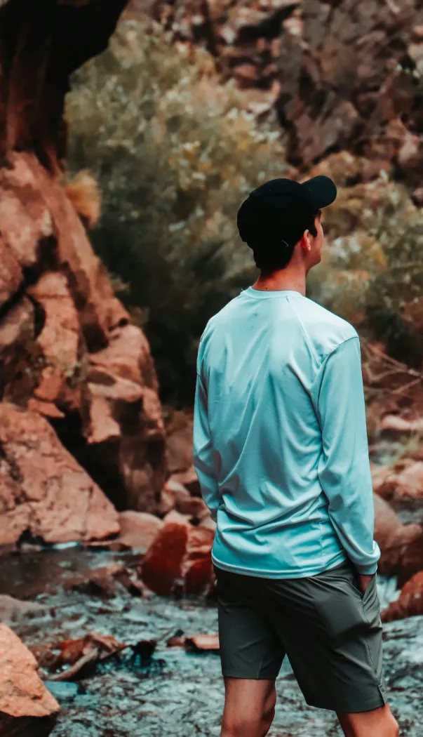 a relaxed young man facing away from the camera looks out over a scene in nature