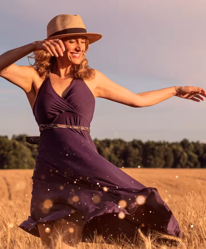 happy woman in a purple dress and a straw hat dancing in a wheat field