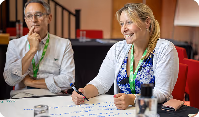 Two professionals collaborate during meeting, smiling and taking notes