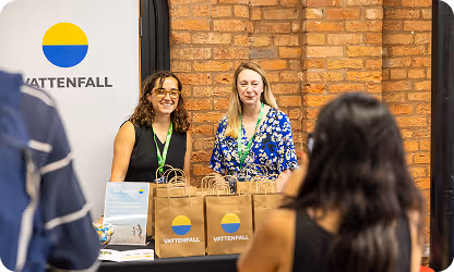 Vattenfall representatives smiling at booth with branded bags and poster
