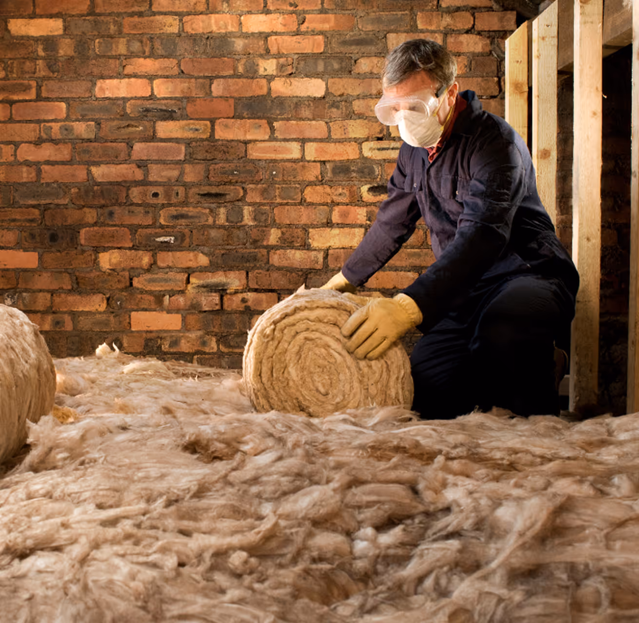 Worker installing wool insulation between brick wall and wooden frame