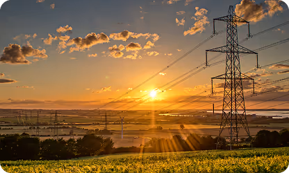 Sunset over field with electric transmission towers and golden sunrays