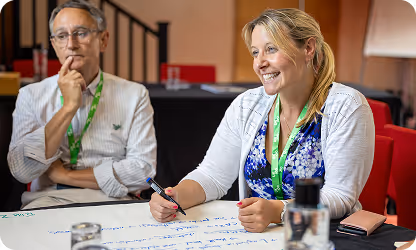 Two professionals smiling and collaborating during a meeting, writing notes