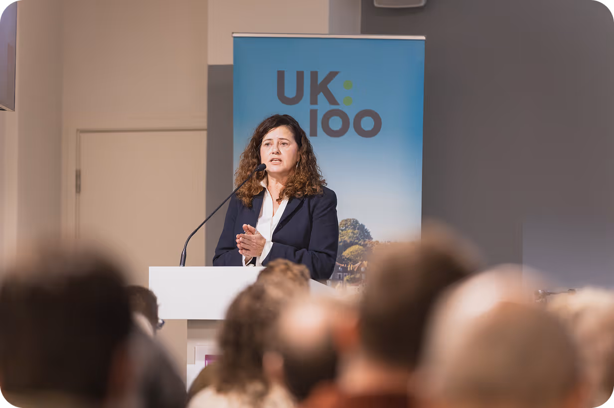 Speaker presenting at UK100 conference with audience in foreground