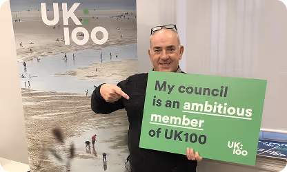 Smiling man holding green UK100 sign about council's ambitious climate goals