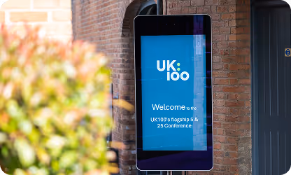 Digital screen displaying UK.log welcome message mounted on brick wall