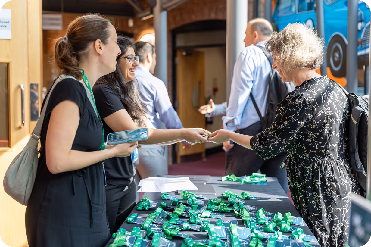 Women exchanging materials at conference registration table with green badges