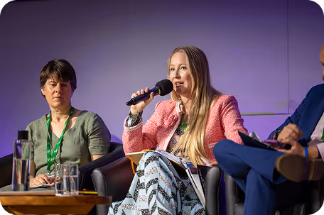 Woman in pink sweater speaks into microphone during panel discussion