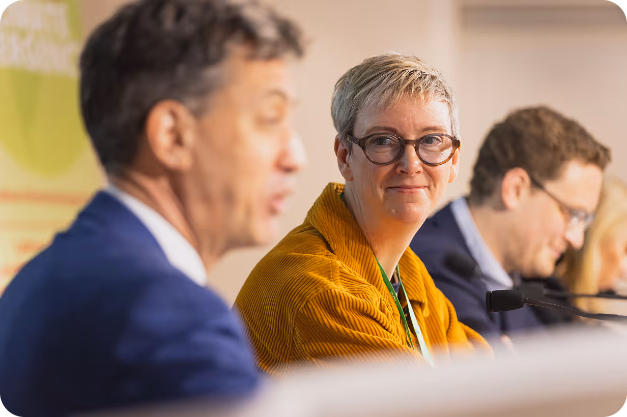 People in professional meeting, woman in yellow cardigan smiling attentively